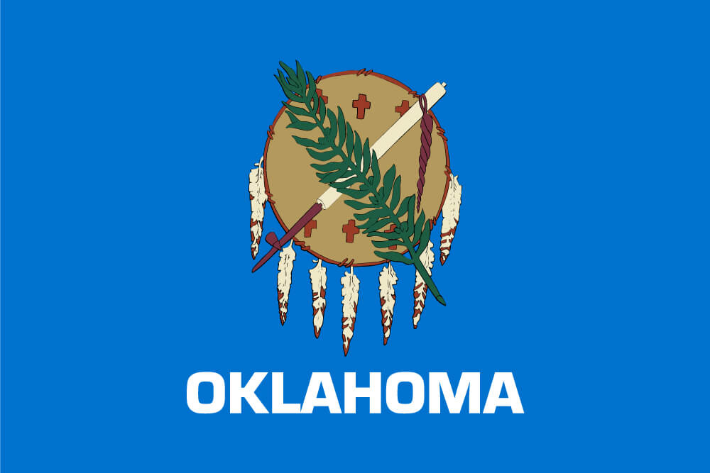 a field of sky blue charged with an Osage war shield, a peace pipe, and an olive branch; “Oklahoma” is inscribed below in white